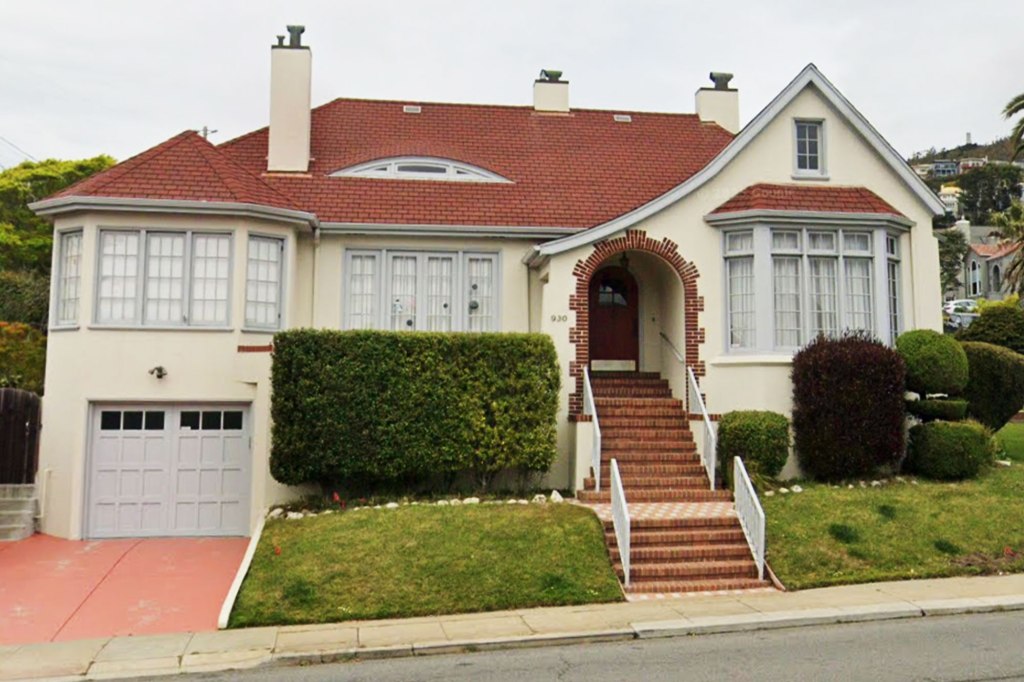 A beige house with a red roof and brick steps leading to the front door, with a red driveway leading to the garage on the left.