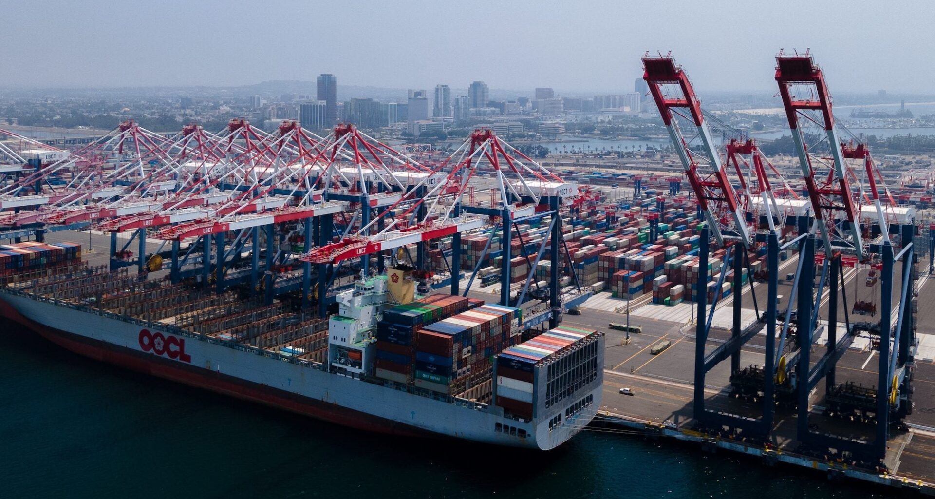 A cargo ship is moored in the Port of Long Beach while cranes retrieve cargo containers from the ship