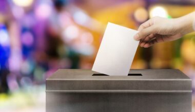 Colorful image of a hand, a white sheet of paper, and a box symbolizing the act of voting