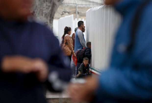 On Tuesday families gather at El Chaparral in Tijuana to add their names to the notebook. The notebook is a list of migrants who have checked in and have been assigned a waiting number.