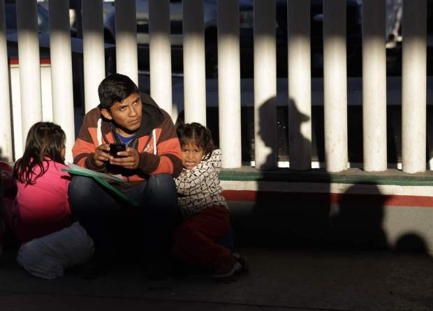 FILE - In this Jan. 25, 2019, file photo, a migrant who did not give his name looks on with his children as they wait to hear if their number is called to apply for asylum in the United States, at the border in Tijuana, Mexico. The Trump administration's effort to make asylum seekers wait in Mexico explicitly targets Spanish-speakers and people from Latin America, according to internal guidelines of a highly touted strategy to address the burgeoning number of Central Americans arriving at U.S. borders. (AP Photo/Gregory Bull, File)