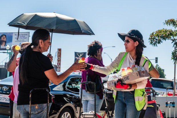 Lupita Guerrero, a volunteer hands out Gatorade that  was donated by Father Joe's to people waiting in line at a food distribution with food from Feeding San Diego at  Iglesia Casa de Alabanza in City Heights  on March 26, 2026. (Ariana Drehsler / For The San Diego Union-Tribune)