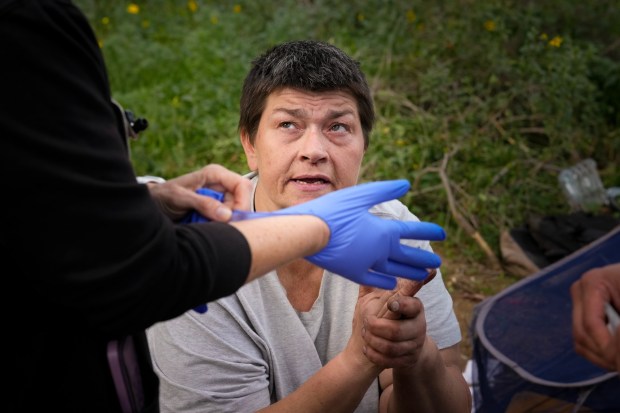 On Monday, March 2, 2026, in San Diego, at an encampment under the Int. 805 bridge, Lisa Silvestro, 52, a nurse practitioner, prepares to examine Micah Munoz, who lives along the San Diego Riverbed with her two dogs. Silvestro is a health professional with Healthcare in Action and offers medical care to those who have become homeless. (Nelvin C. Cepeda / The San Diego Union-Tribune)
