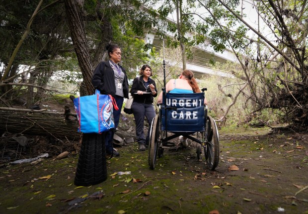On Monday, March 2, 2026, at an encampment along the San Diego Riverbed, Lisa Silvestro (r), 52, a nurse practitioner, and Prizma Mercado (l) check in on their afternoon appointment with Kirstie Ann Moss, 51. Moss, who has been homeless for more than three years, recently was injured in an accident. Silvestro and Mercado are health professionals with Healthcare in Action and offer medical care to those who have become homeless. (Nelvin C. Cepeda / The San Diego Union-Tribune)