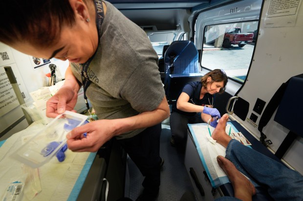 Lisa Silvestro (r), 52, a nurse practitioner, examines a man's foot while Prizma Mercado (l) looks over the exam tray. Silvestro and Mercado are health professionals with Healthcare in Action and offer medical care to those who have become homeless. (Nelvin C. Cepeda / The San Diego Union-Tribune)