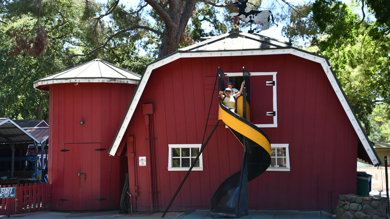 A woman and child go down a slide coming out of a red barn