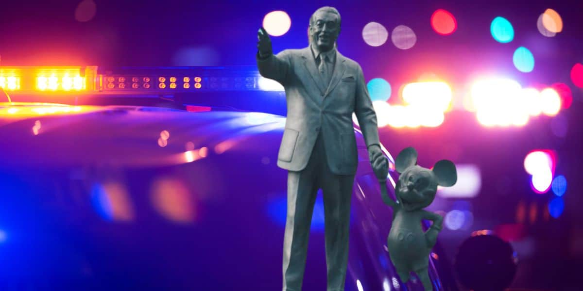 The Walt and Mickey statue holding hands with police lights in the background in Orlando.