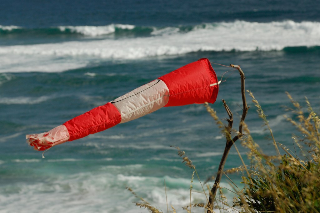 A red and white windsock indicating wind direction next to a beach with ocean waves.