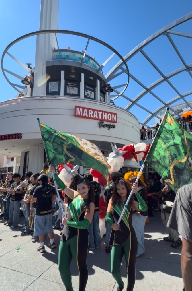 Two women in green and black uniforms holding flags, with a "Marathon Burger" sign and a crowd in the background.