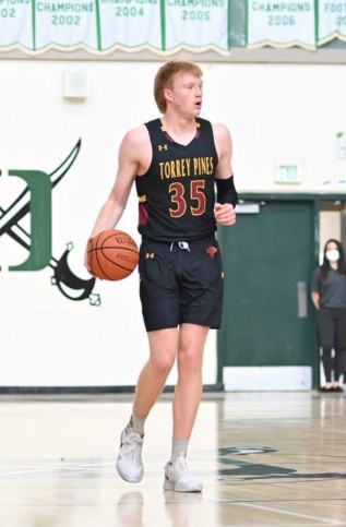 A tall man in a uniform with a basketball in his right hand on a court.