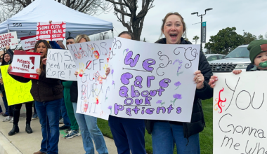 Bakersfield nurses holding signs along street "We care about our patients" "Hands off our burn unit" "Some cuts don't heal"