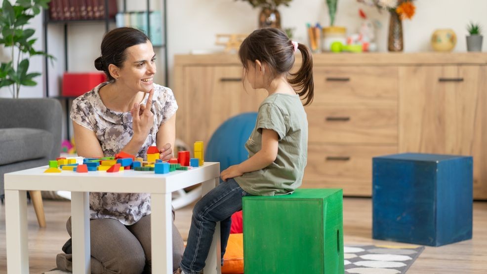 The woman appears cheerful, possibly praising the child during a block building exercise beneficial for motor skills development and aligned with speech therapy or psychologist strategies