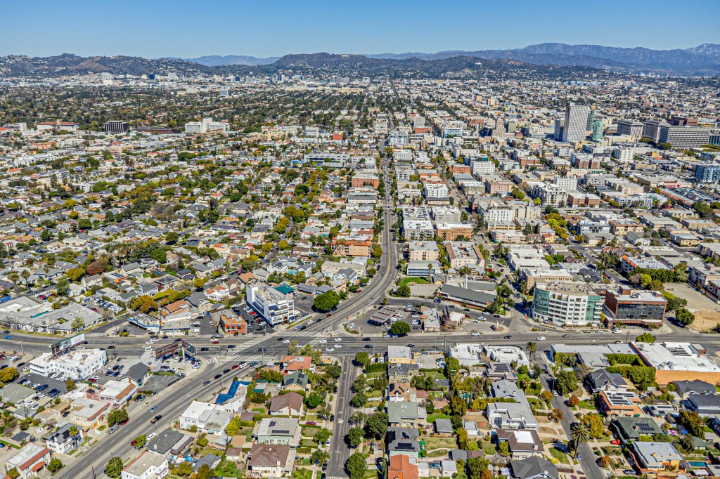 Aerial drone view of Koreatown, Los Angeles, California, with residential and commercial buildings, streets, and mountains in the distance.