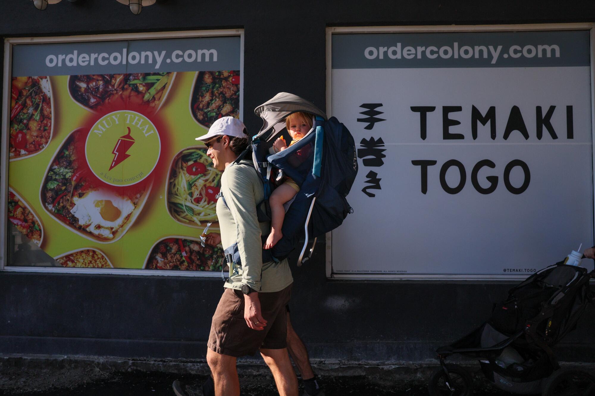 A man walks with his daughter in a hiking backpack.