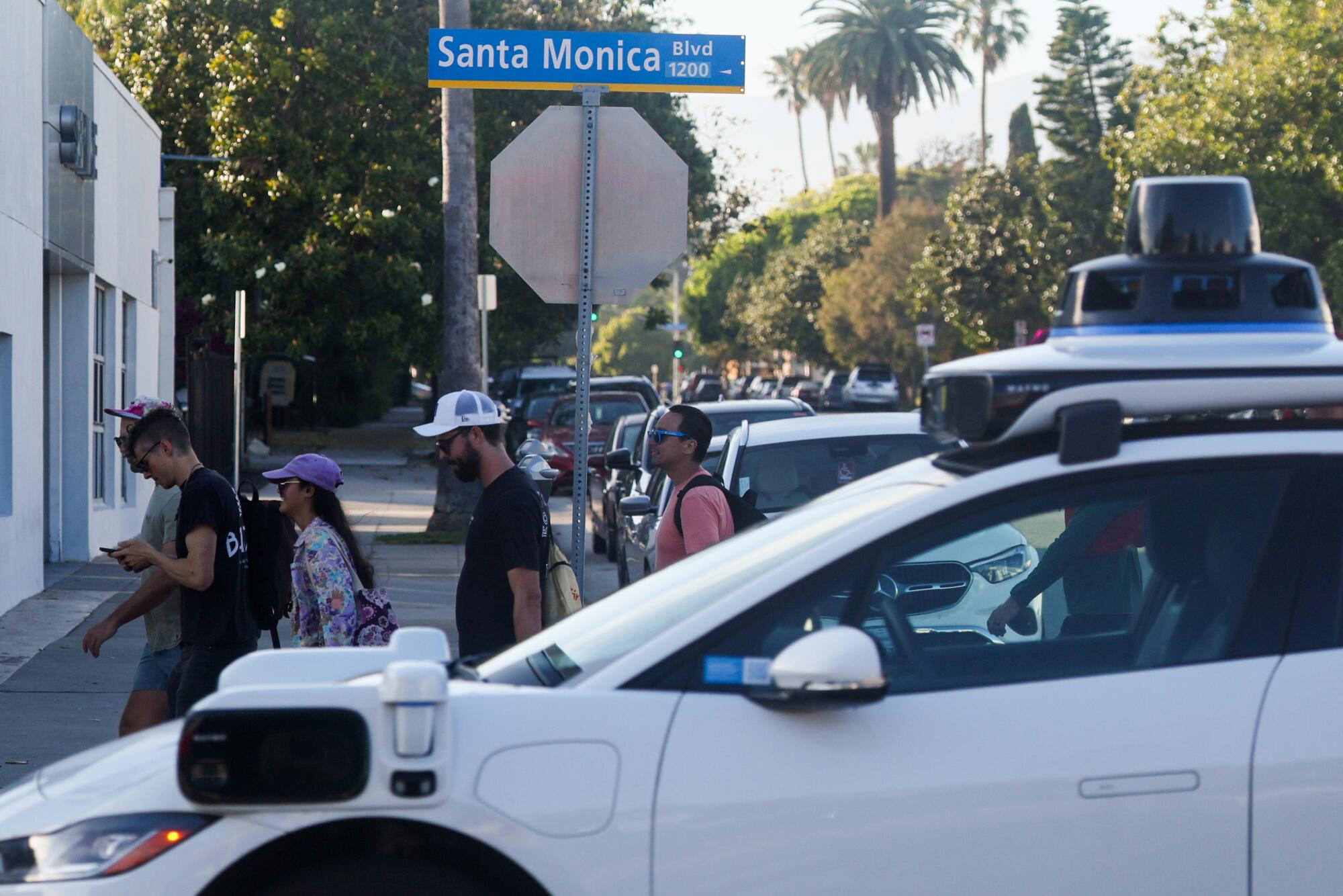 A self-driving Waymo passes a large group walking down Santa Monica Boulevard.