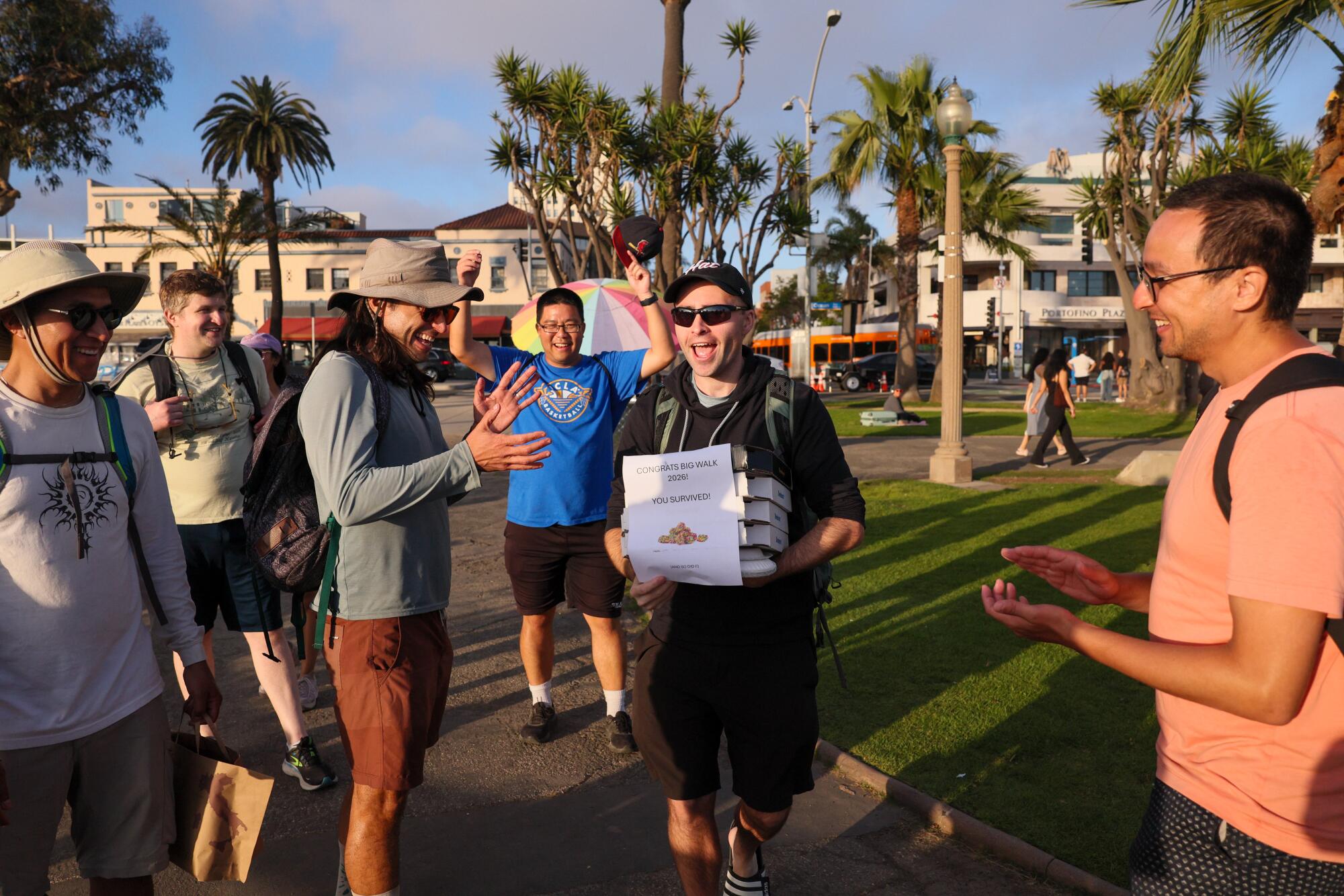 A man holds pizza boxes as people clap nearby.