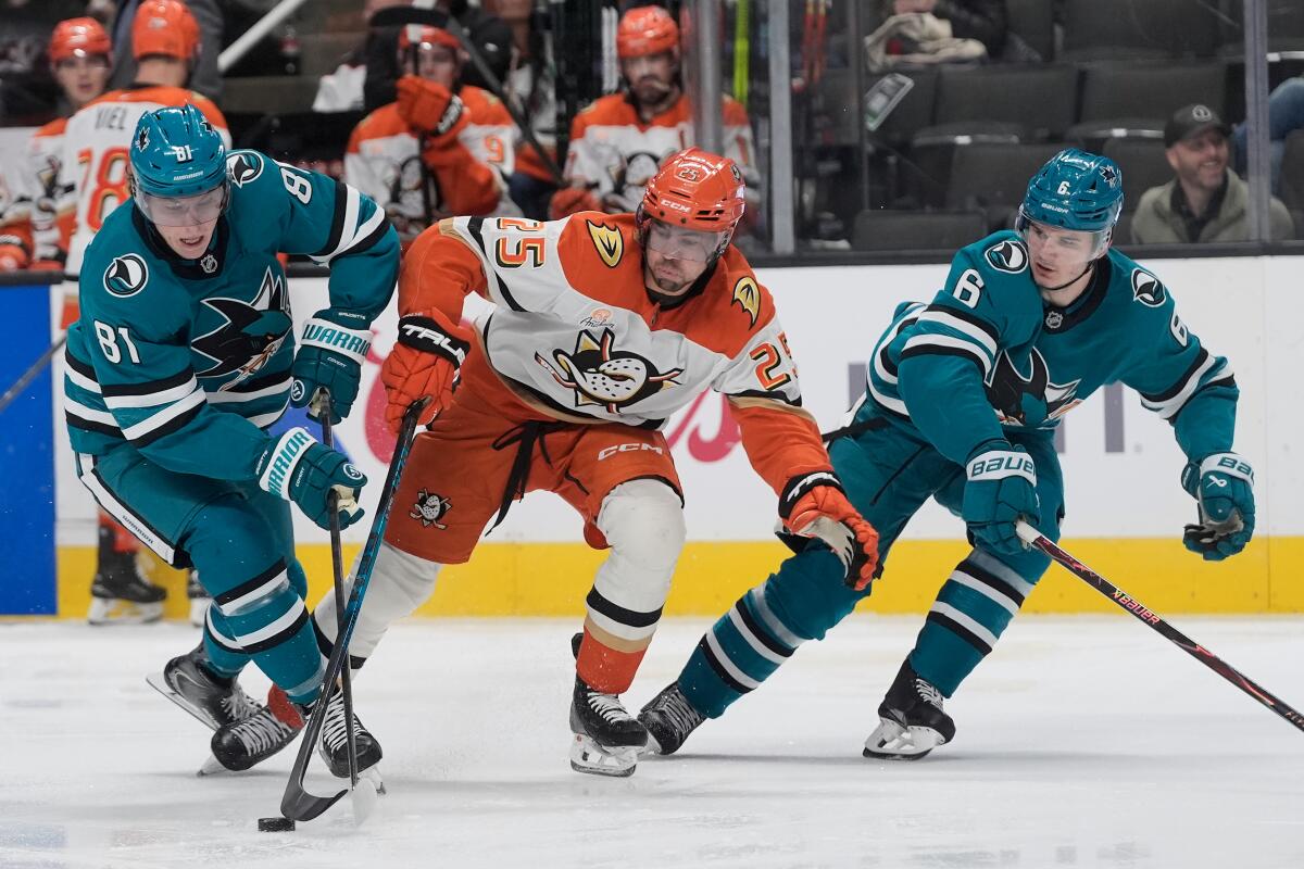 Ducks forward Ryan Poehling skates toward the puck between Sharks forward Adam Gaudette, left, and defenseman Sam Dickinson.