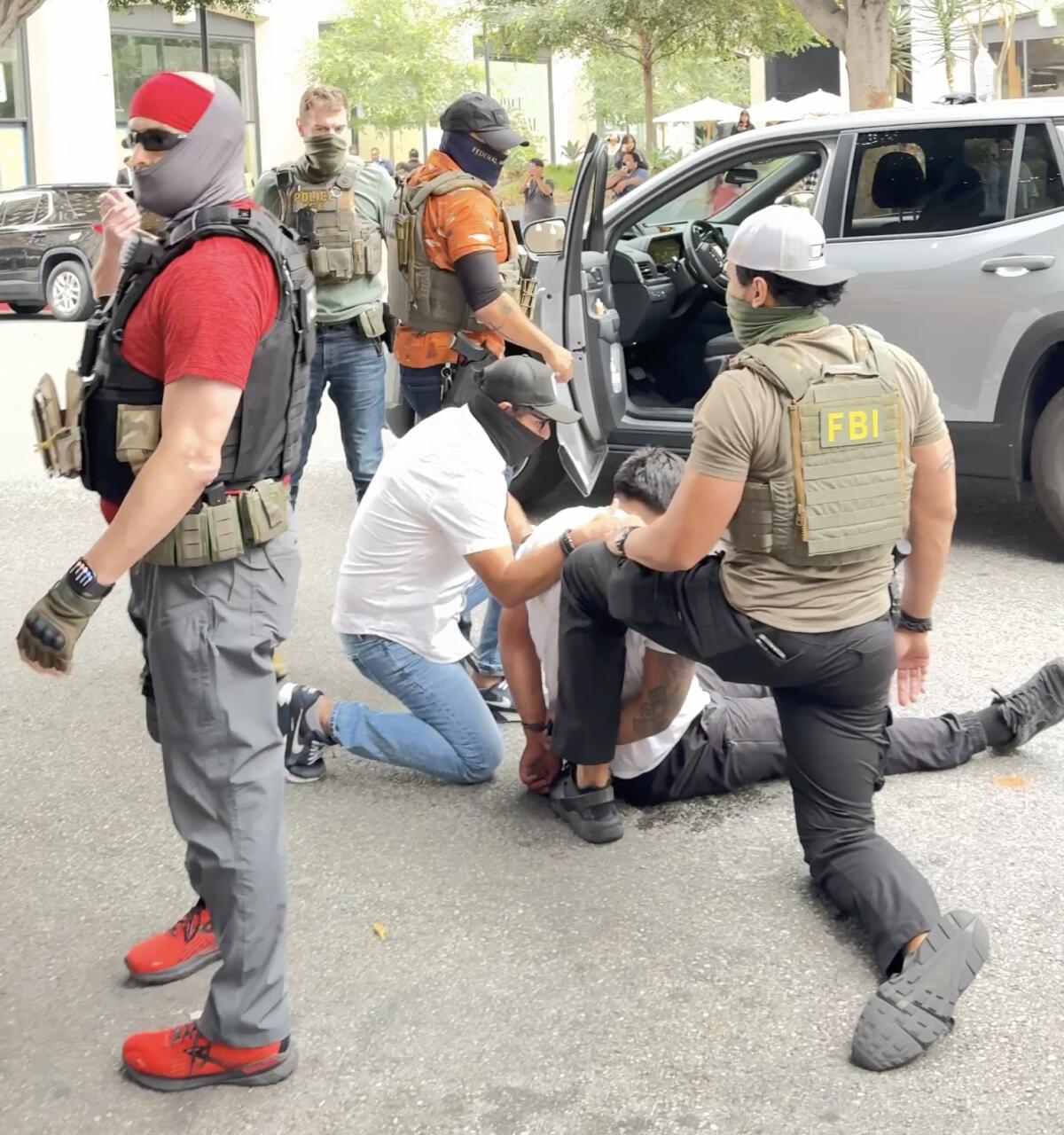 Masked, plainclothes agents take Luis Hipolito into custody after wrestling him to the pavement.