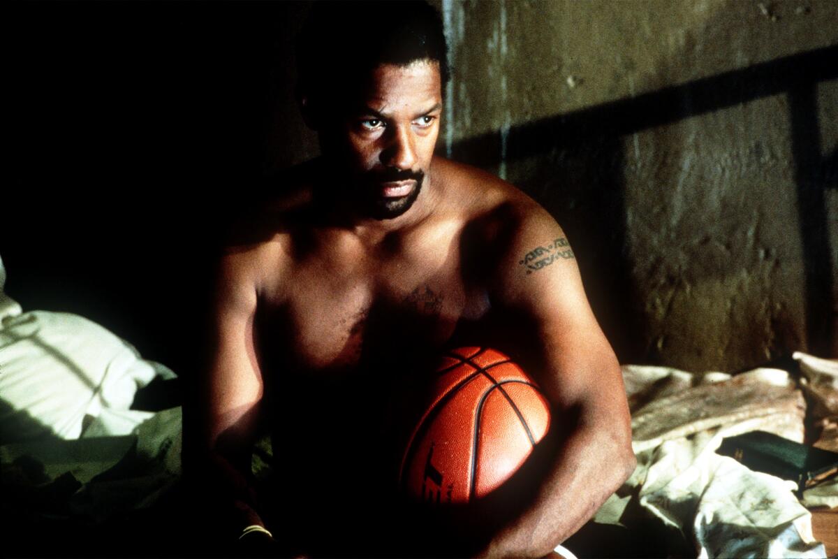 A shirtless man sits with a basketball under his arm.