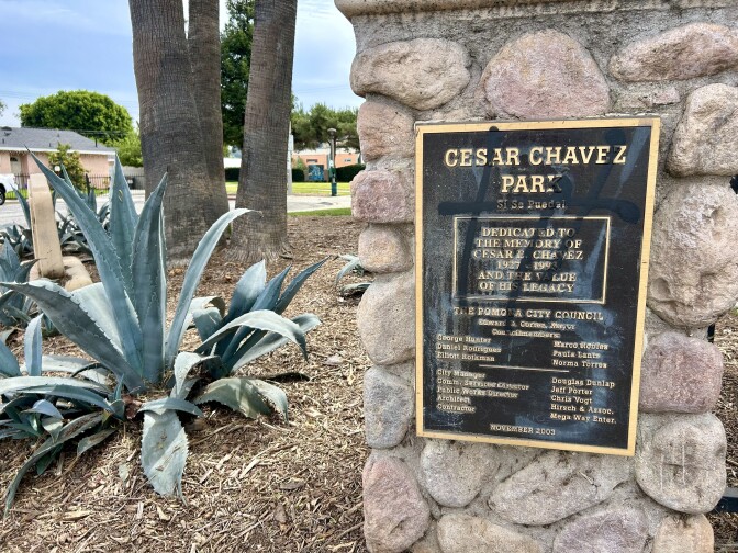 A bronze plaque next to plants and trees says, "Cesar Chavez Park"