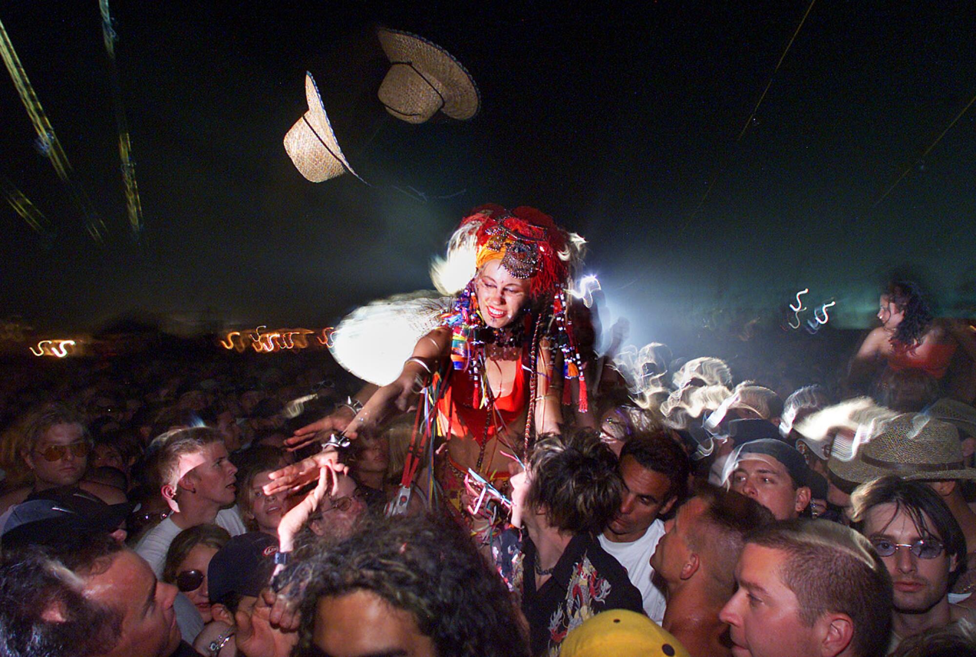 A person in a costume on stilts walks through a crowd of people as straw hats are tossed in the air
