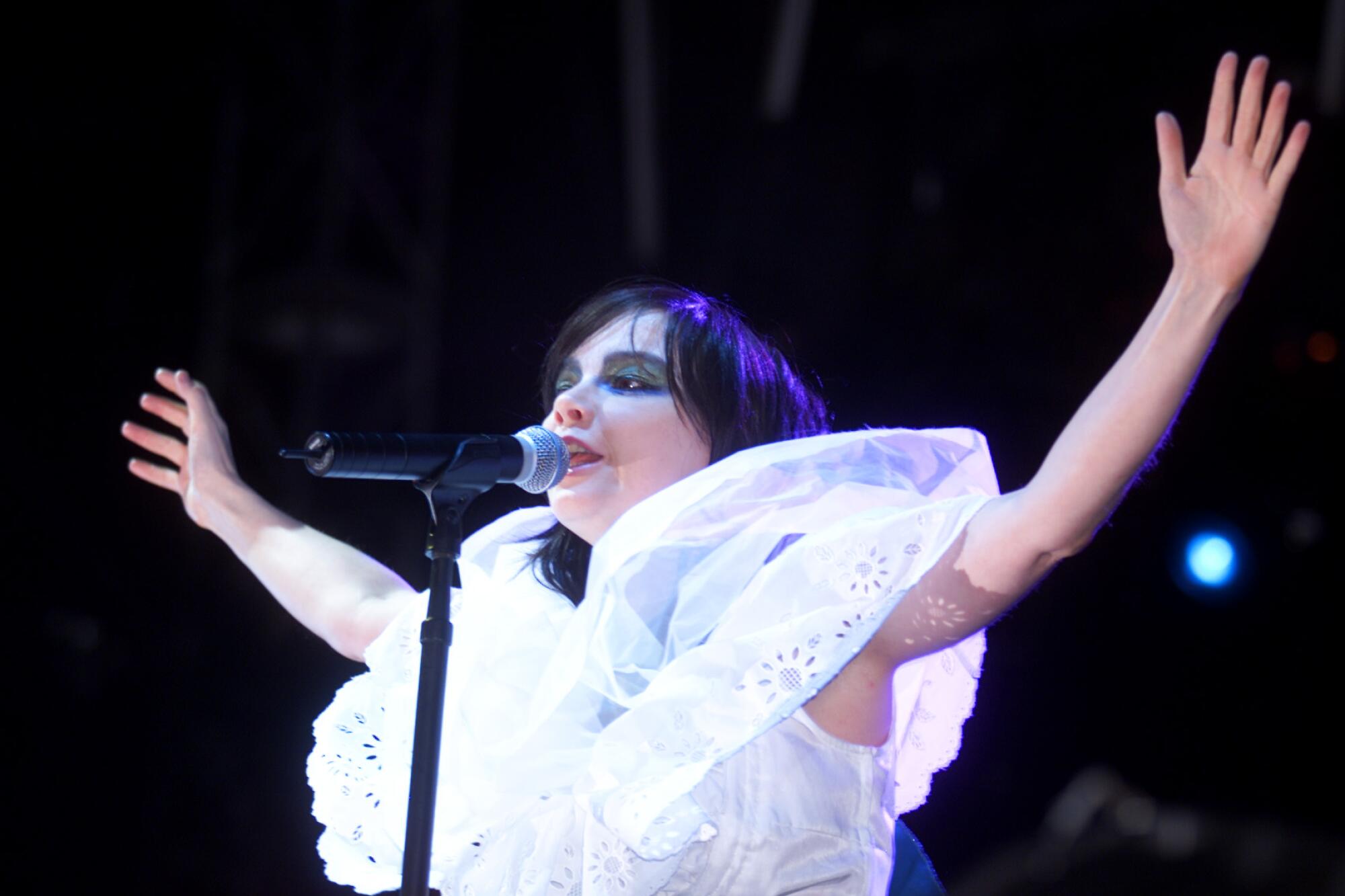 Bjork, wearing a white dress, sings with her arms outstretched