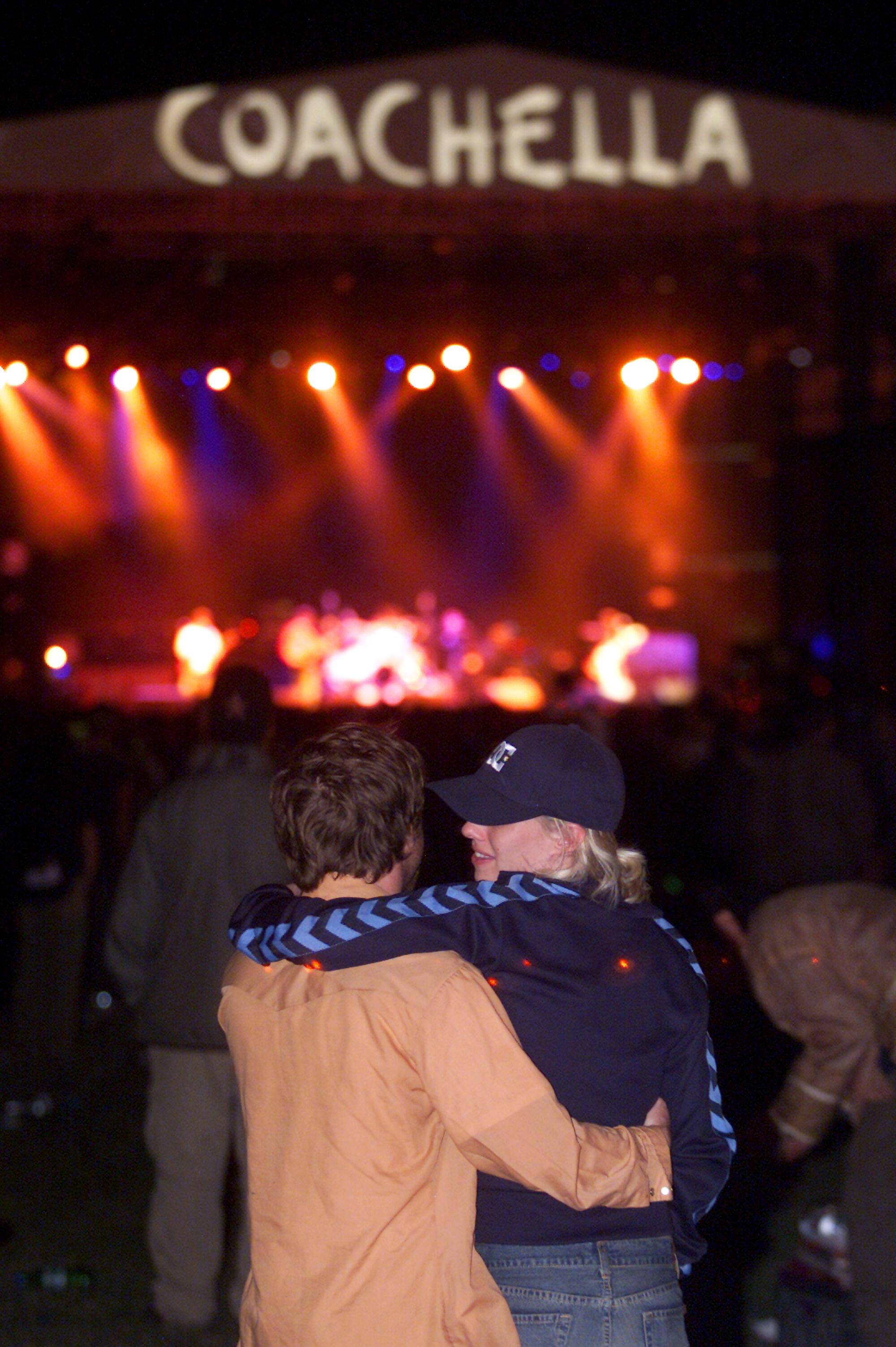 Two fans watch a band on a stage labeled Coachella