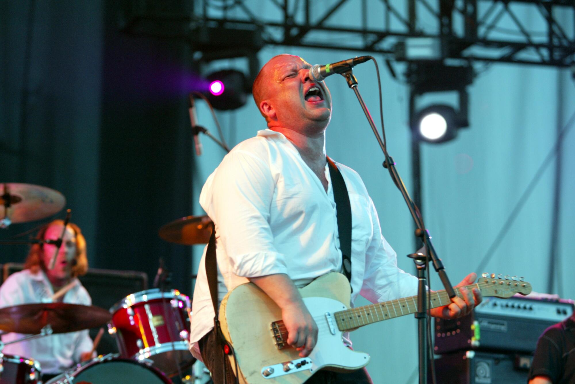 Frank Black wears a white shirt while he plays guitar and sings into a microphone.