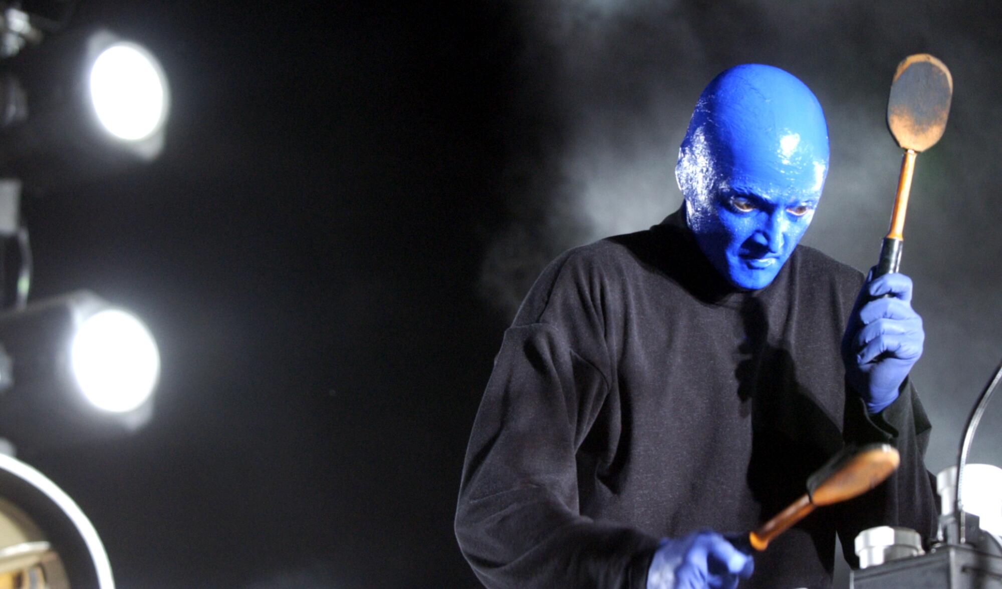Blue Man Group member holds two percussive spoon paddles