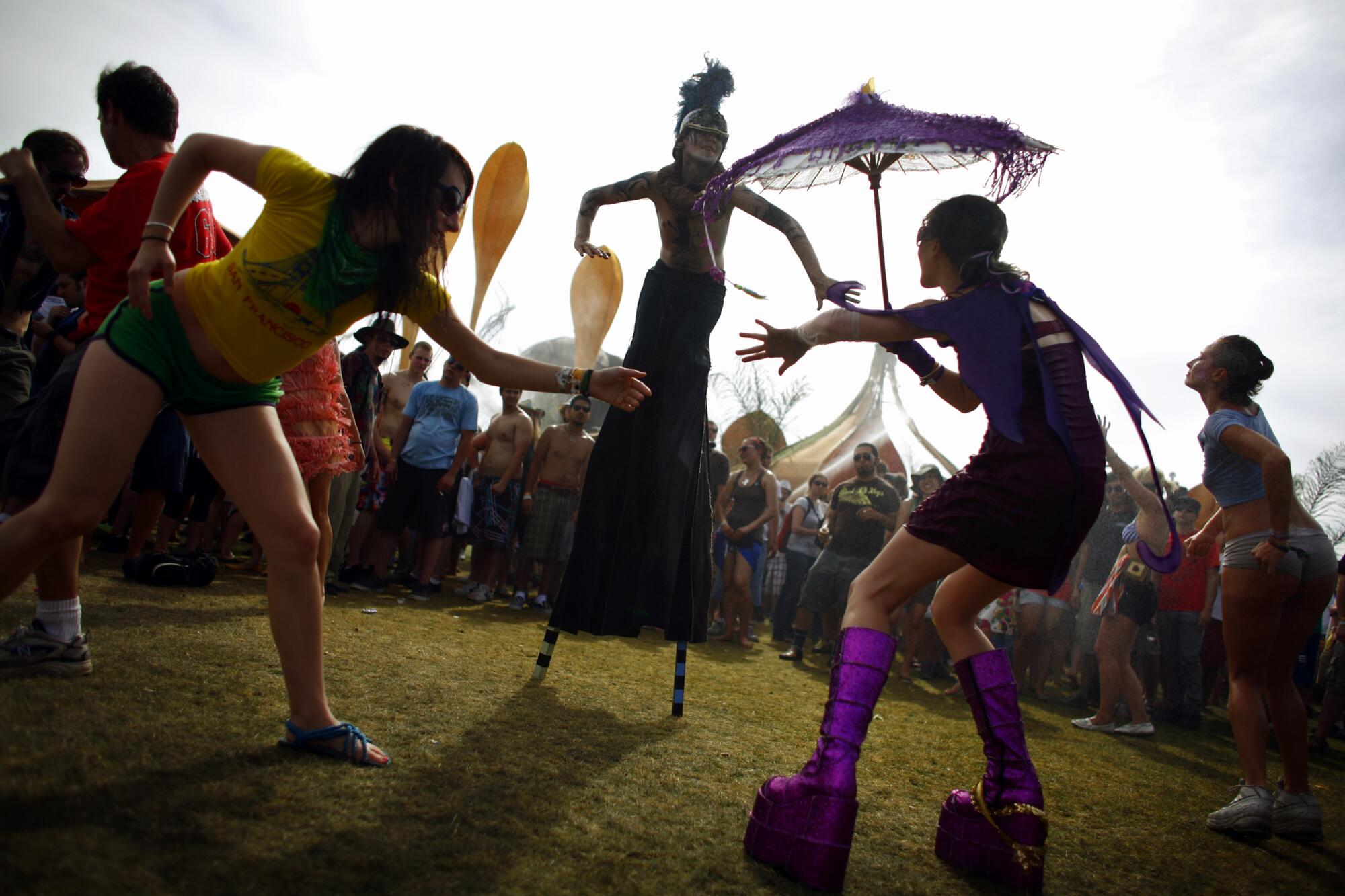 People dance around a person wearing stilts