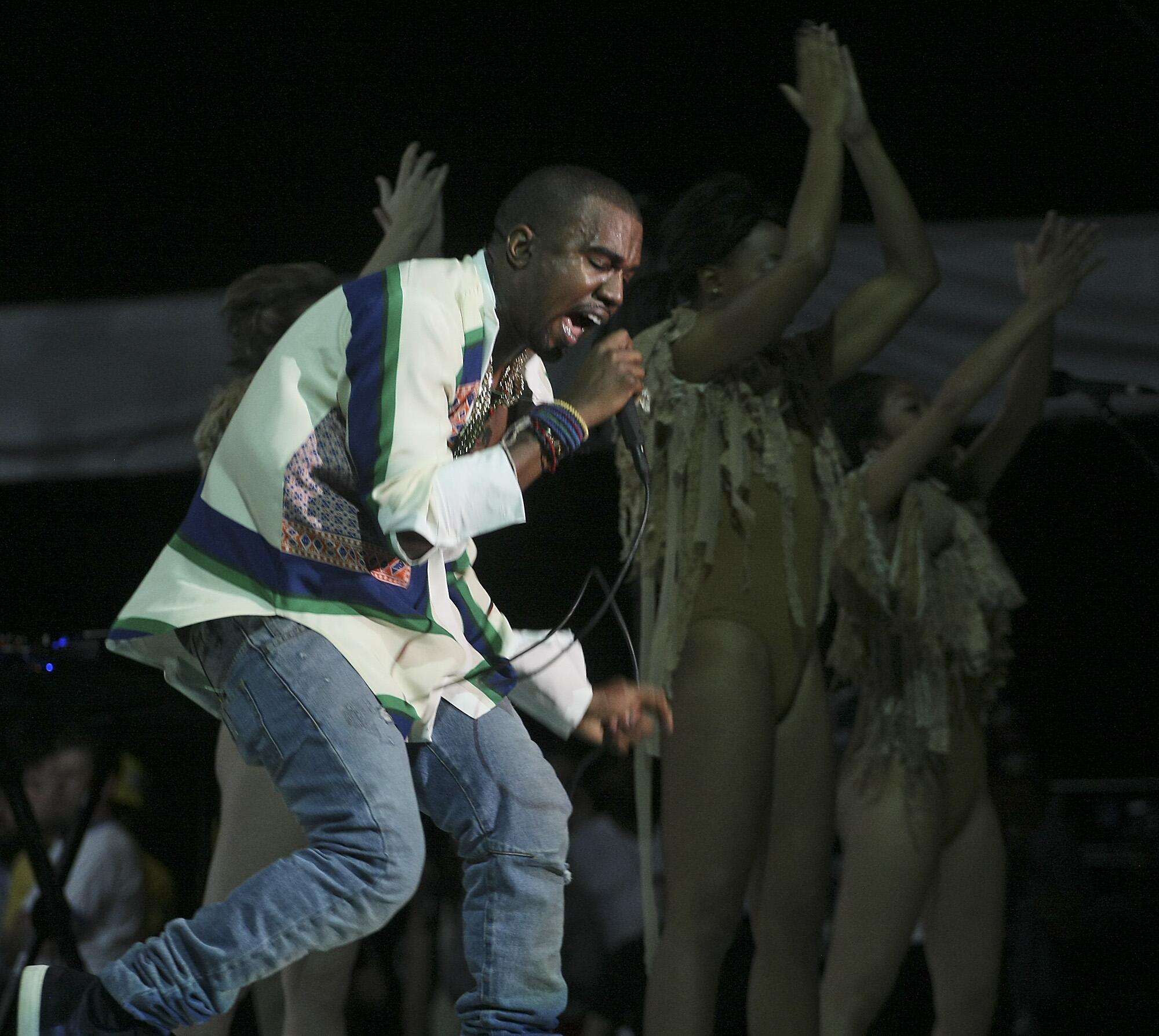 Kanye West raps into a microphone with dancers behind him