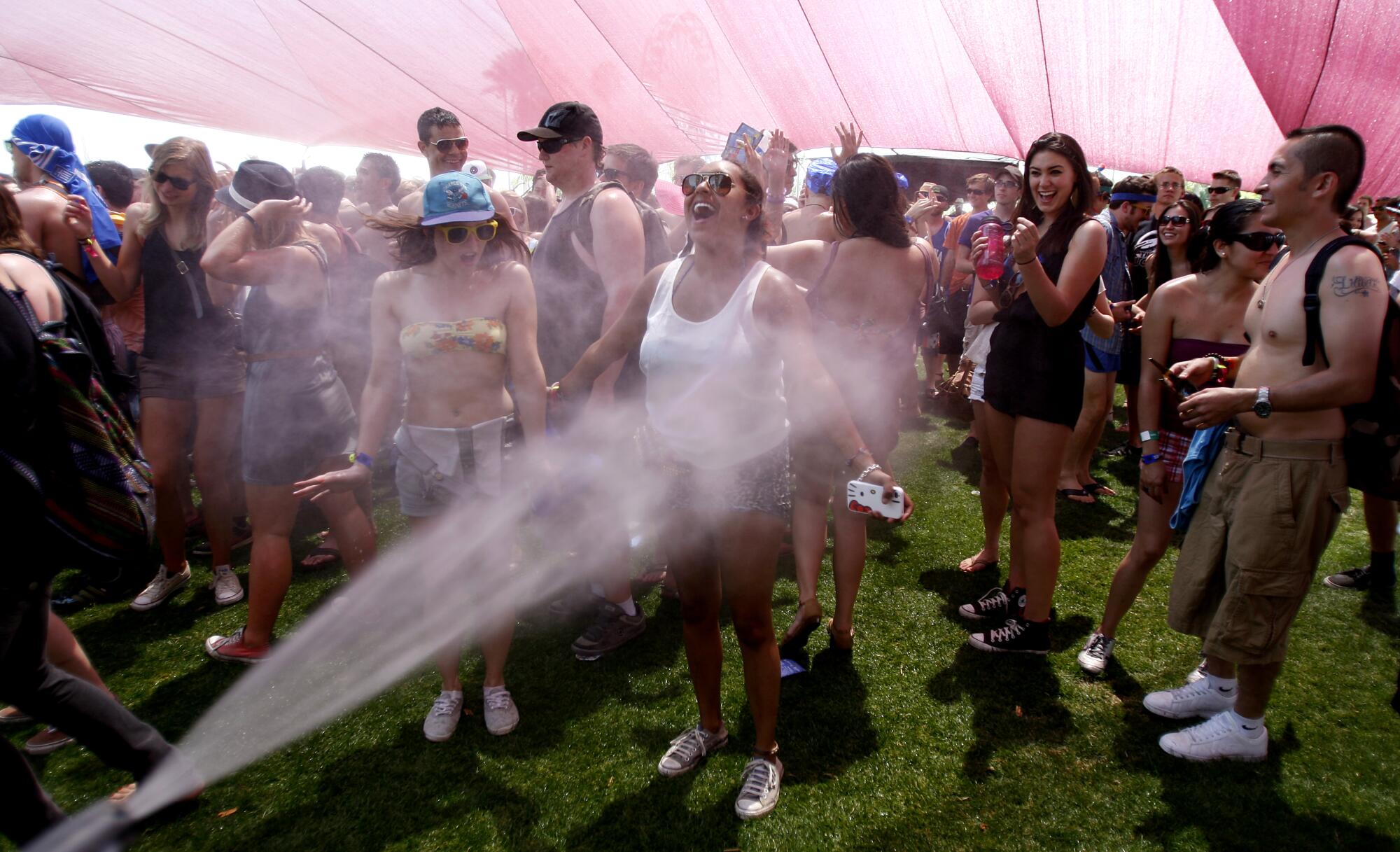A woman gets sprayed with water while other people cool off in the shade at Coachella