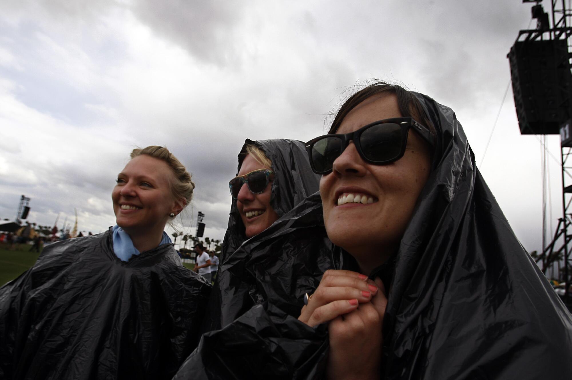 Three women wear rain gear and two have sunglasses at coachella