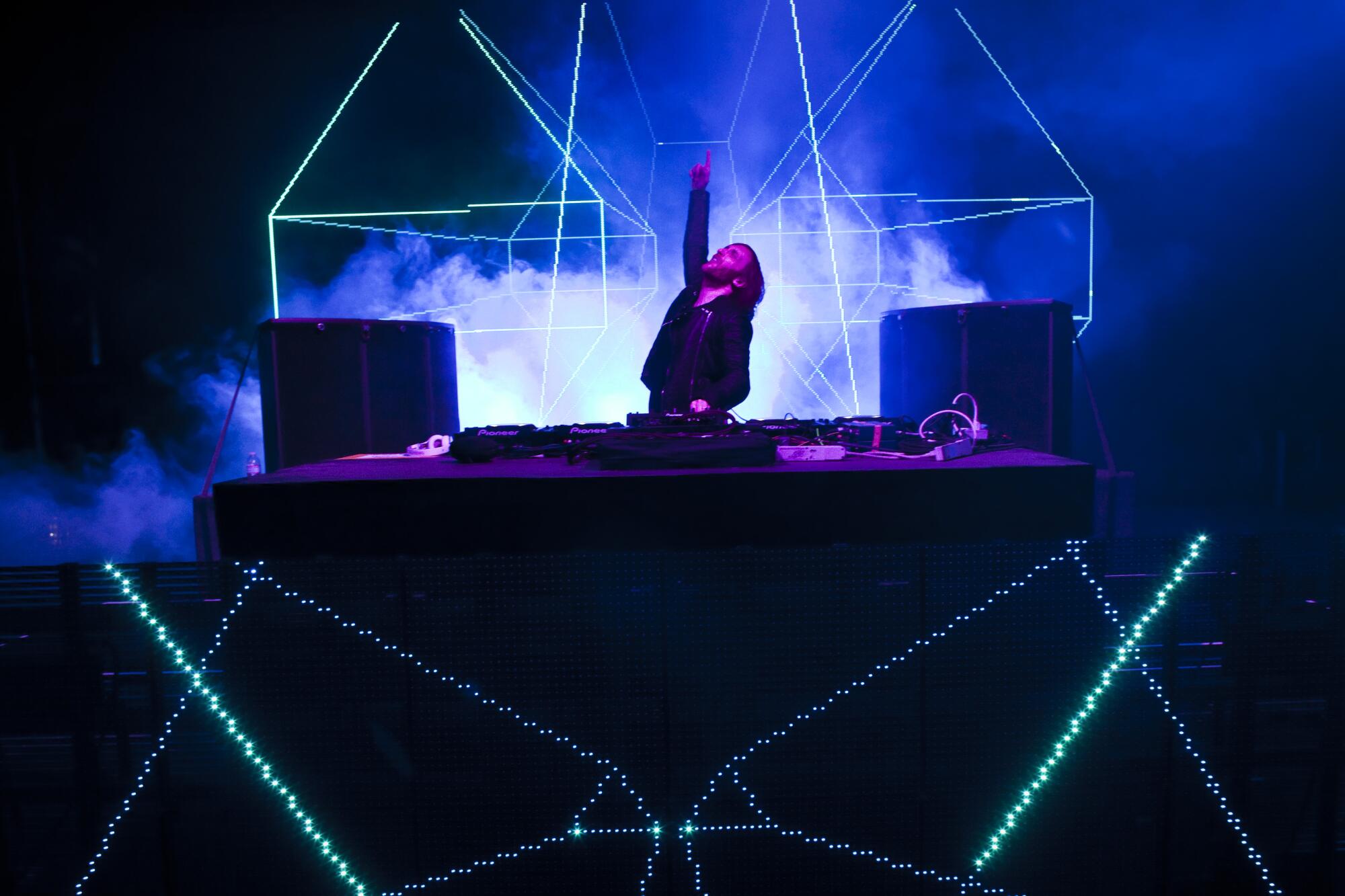 David Guetta behind his DJ setup with lasers and pointing his finger in the air