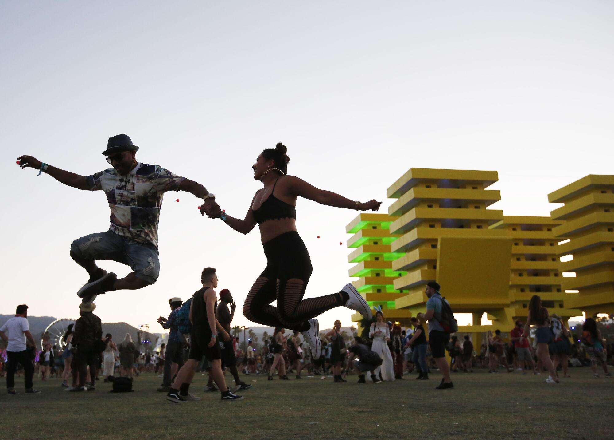 two people hold hands and jump in front of a large yellow sculpture