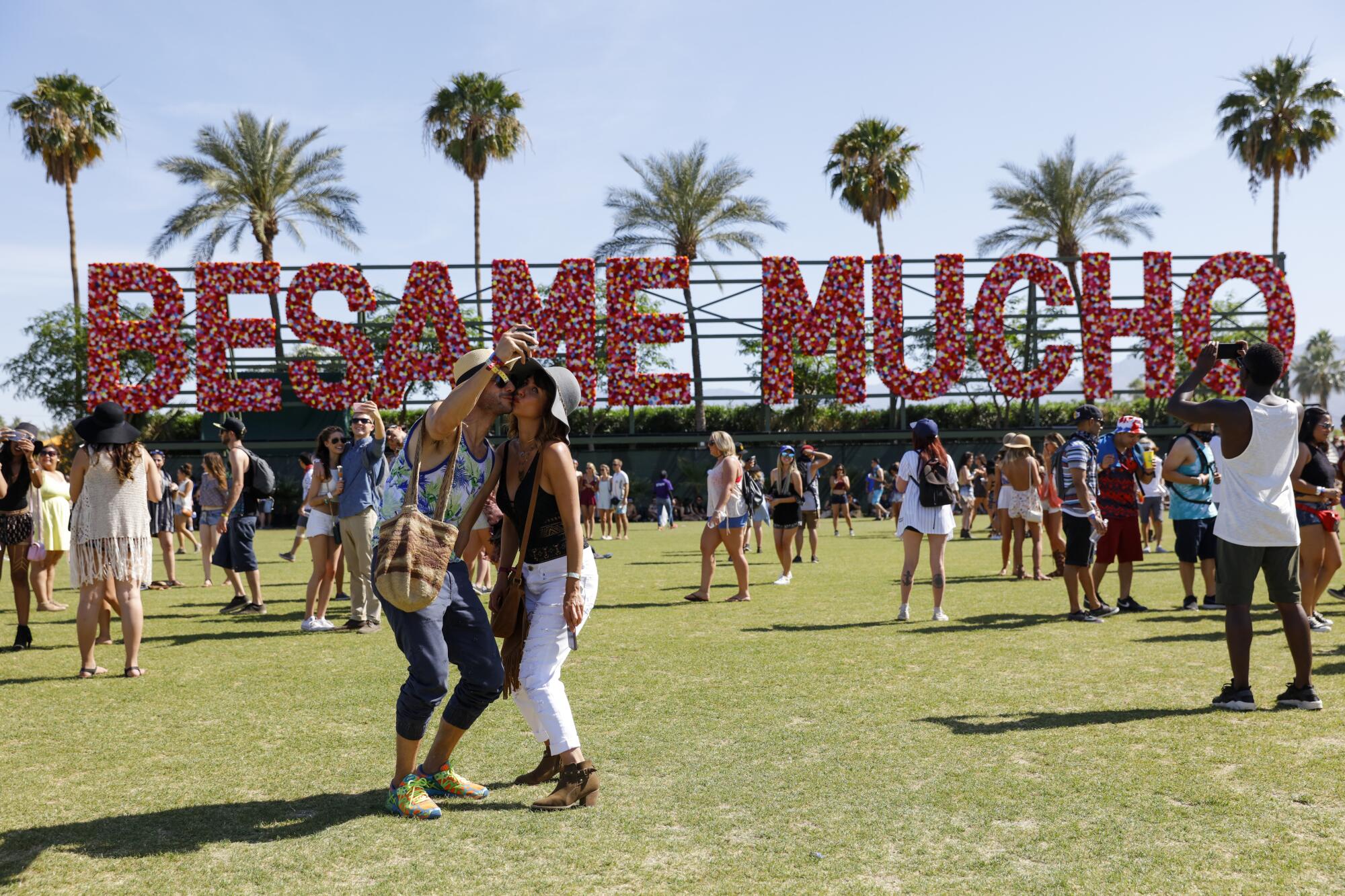 people pose for a selfie in front of a sign that says "Besame Mucho" made of flowers