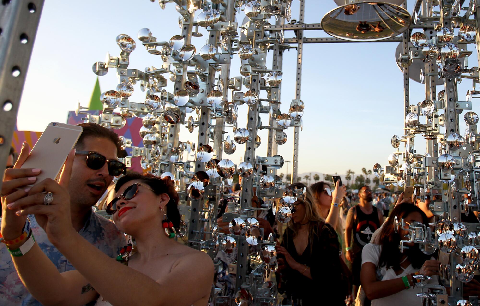 People take photos in a mirrored art installation at Coachella during sunset