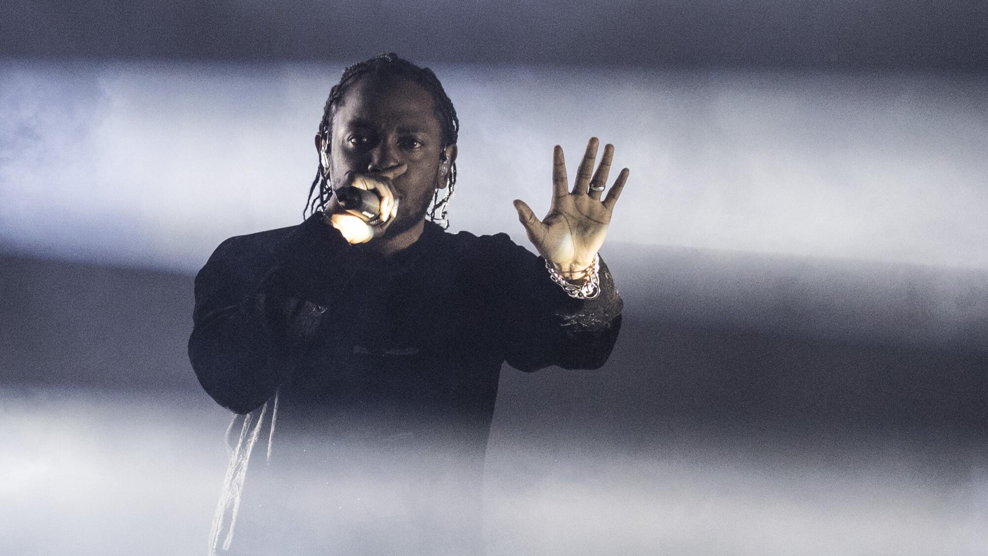 Kendrick Lamar holds a microphone and has his other palm out