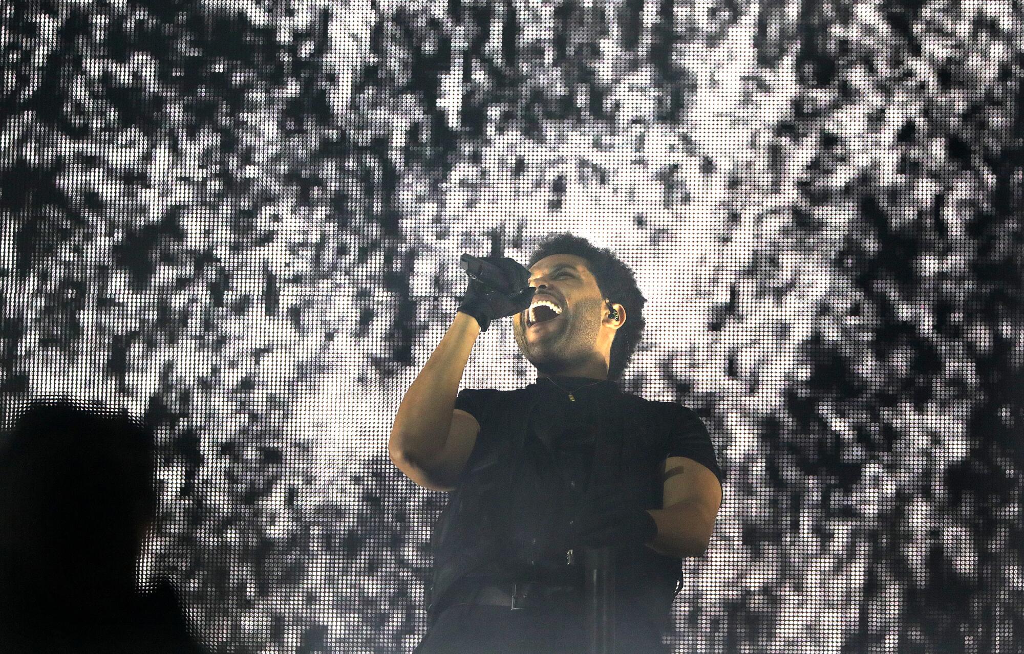 The Weeknd wears gloves and leans back as he sings into a microphone