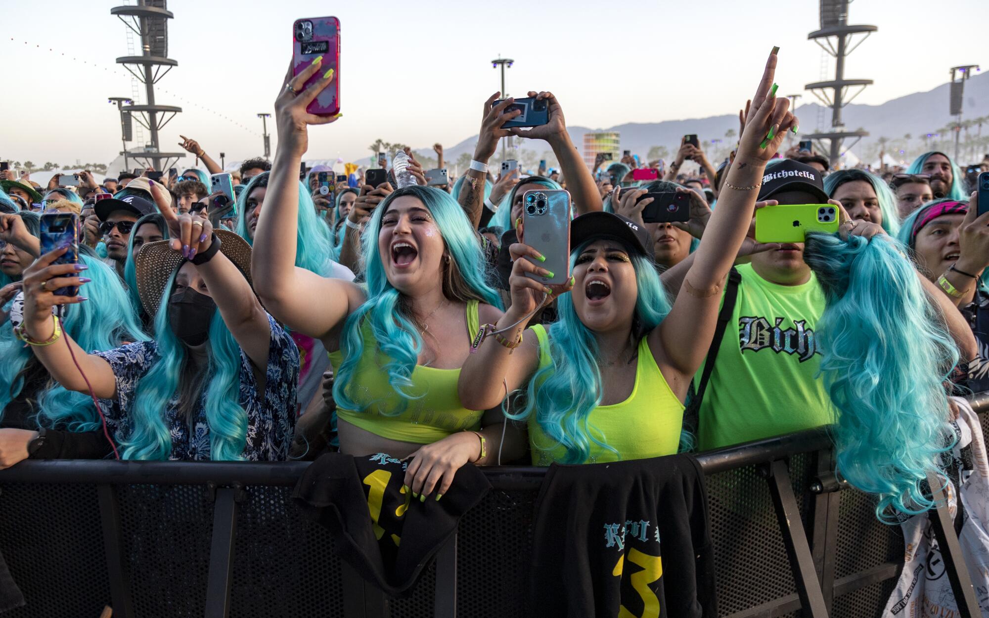 Fans in the front row wear turquoise wigs and take photos