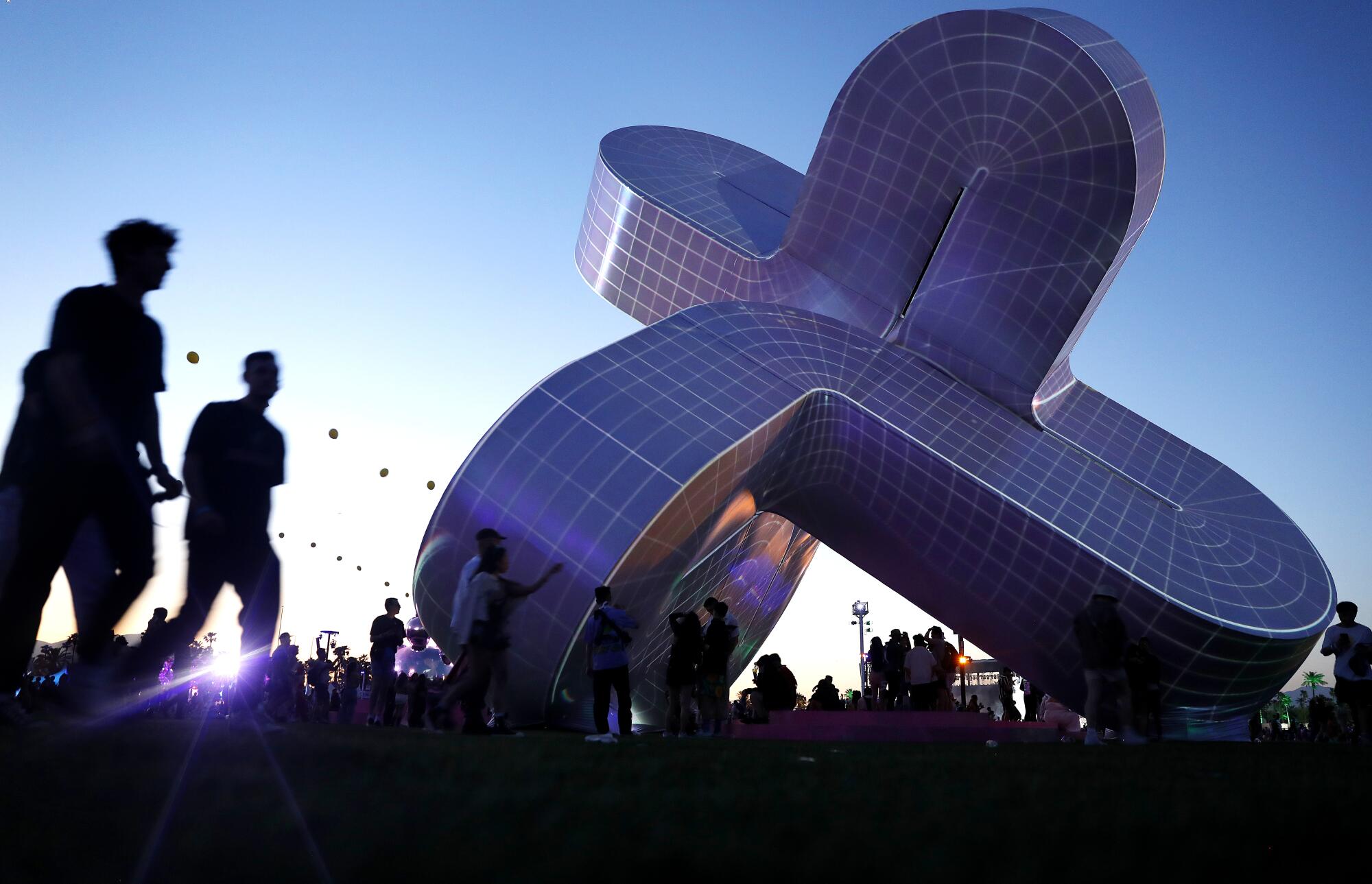 People walk by an X-shaped art piece at dusk