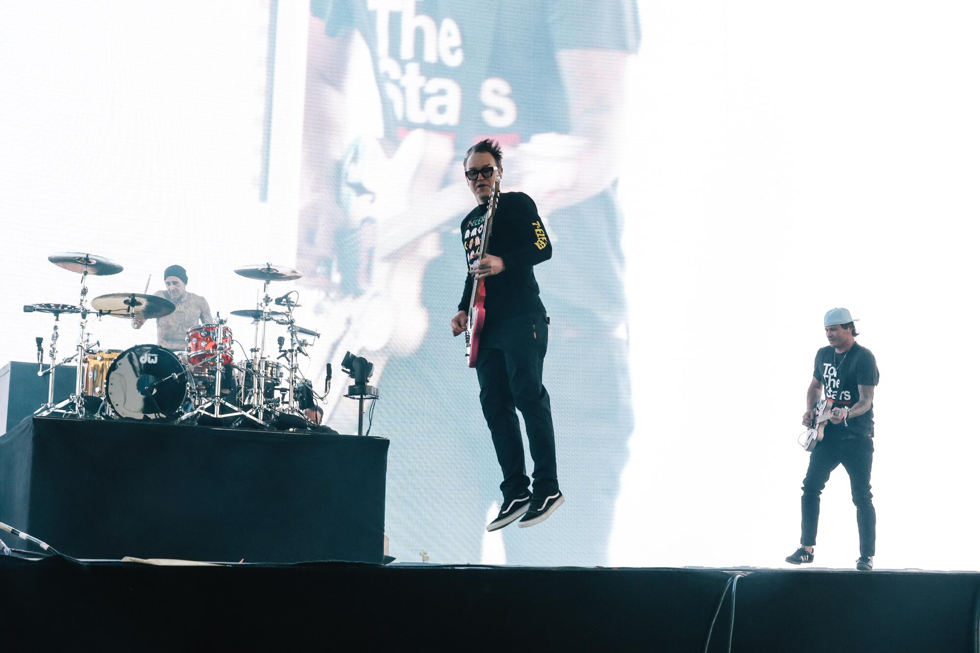Blink-182 plays on a stage. Mark Hoppus is mid air