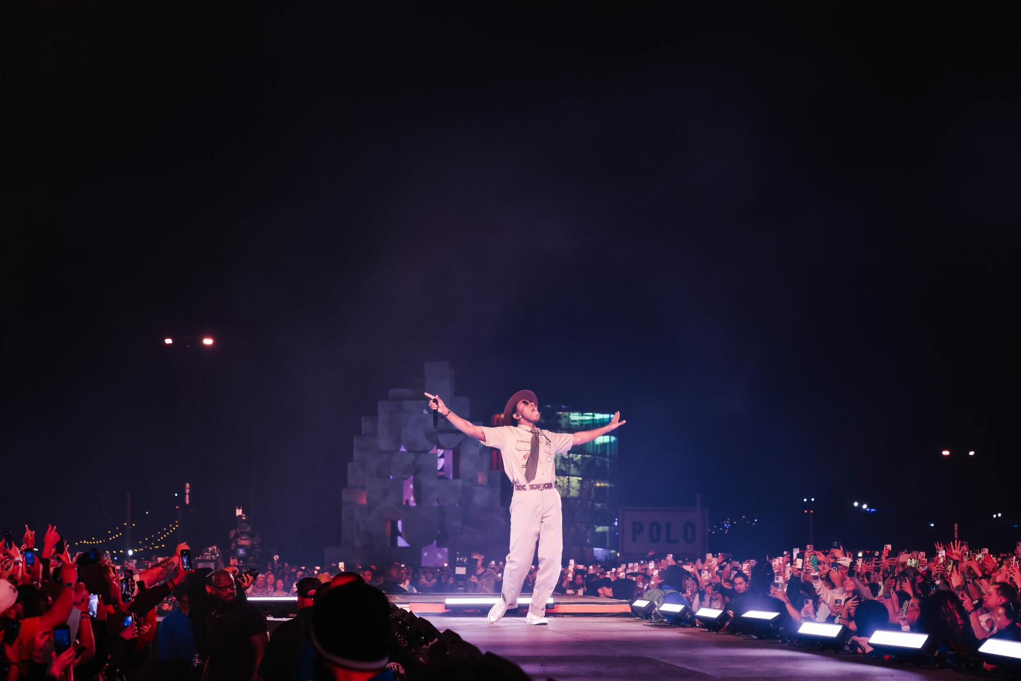 Tyler, the Creator, dressed as a park ranger, holds his hands out on the catwalk of a stage