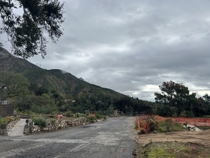 A street extends into the distance along the slope of a mountain. Dirt lots are on either side. 