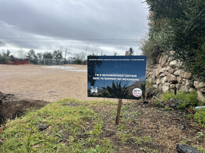 A sign at the edge of a dirt lot reads "I'm a neighborhood captain here to support my neighbors" 