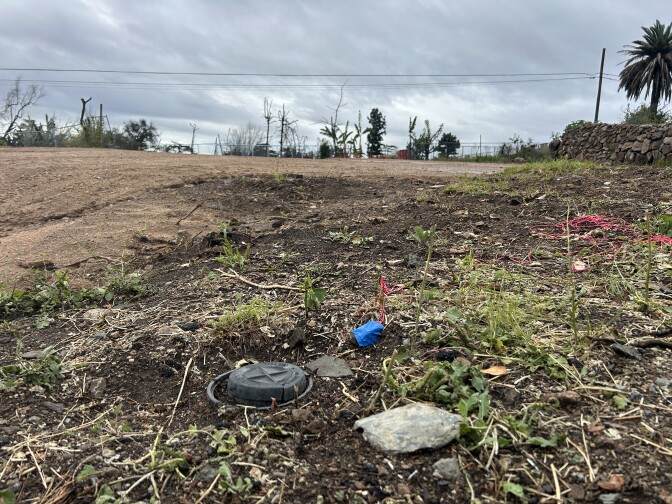 A small black cap in the dirt of an empty lot under overcast sky. 
