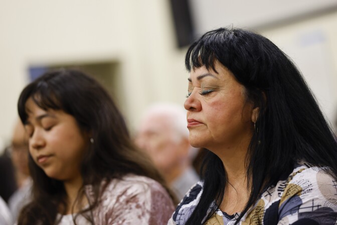 Two women with dark hair and medium skin tone sit together, eyes closed.