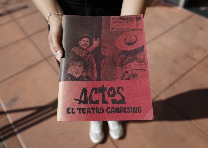 A program that says "Actos: El Teatro Campesino" held in a pair of hands.