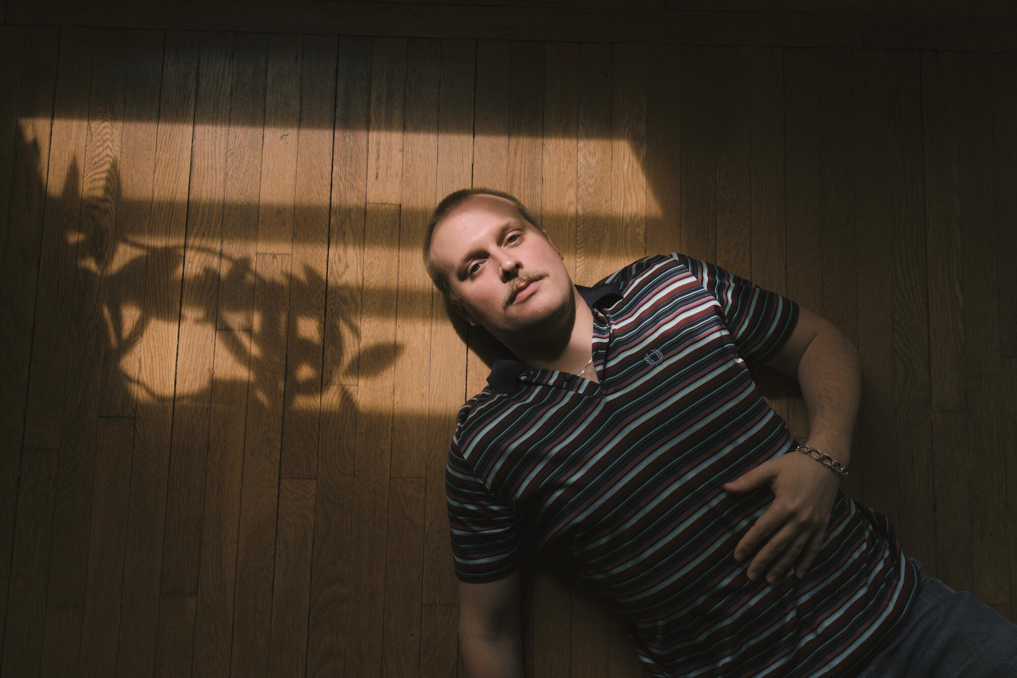 A man lies on the floor of an apartment next to the shadow of a plant.