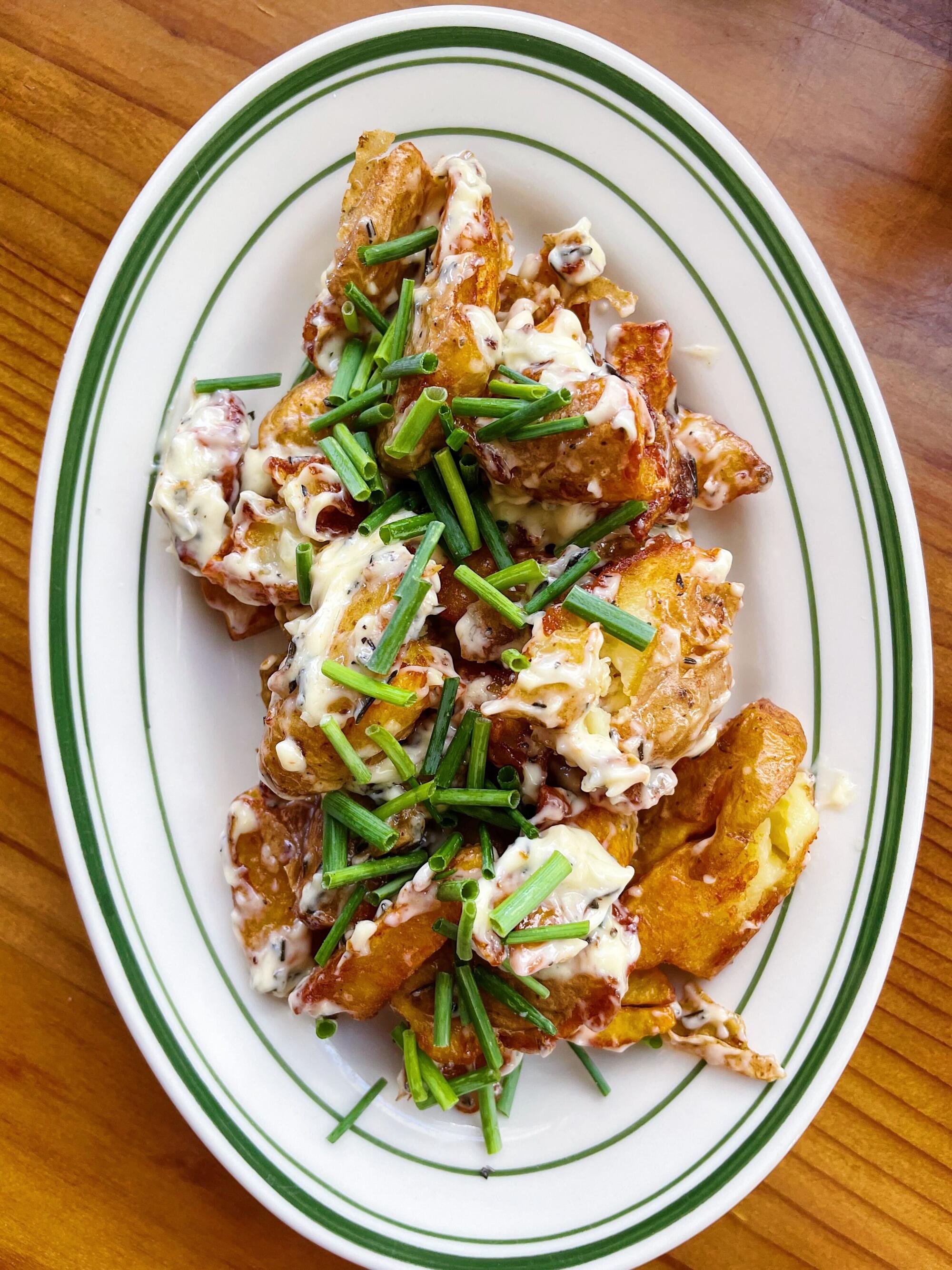 A white and green plate of fried potatoes covered in chives on a wood table
